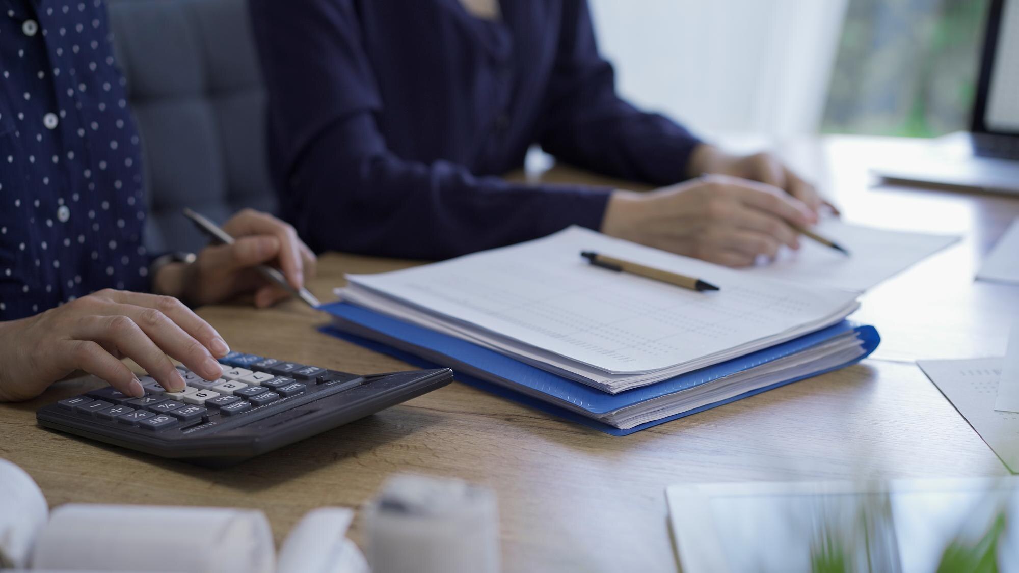 A person reviewing financial documents with a calculator at a desk