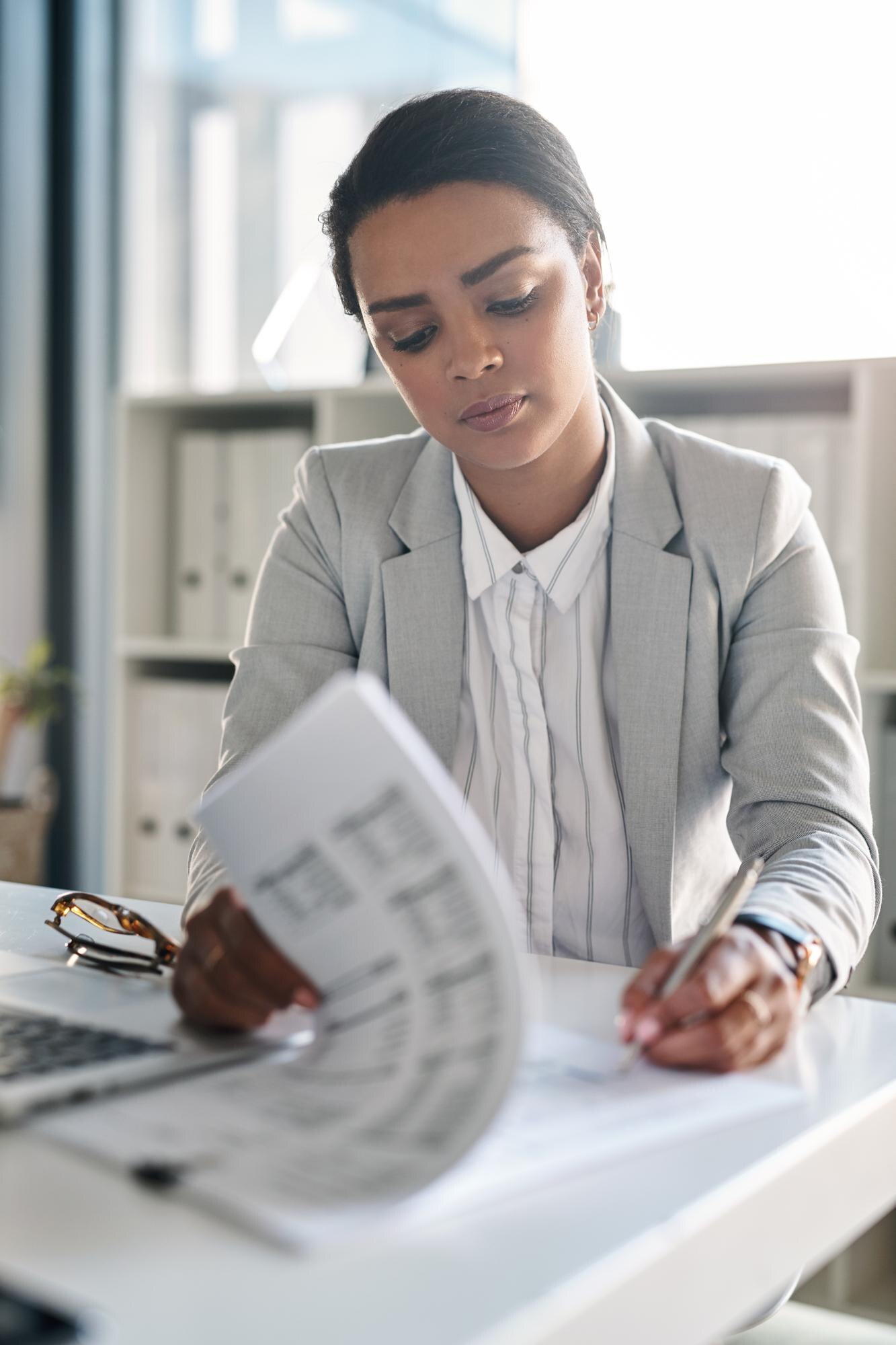 A person at a desk reading through printed documents, pen in hand
